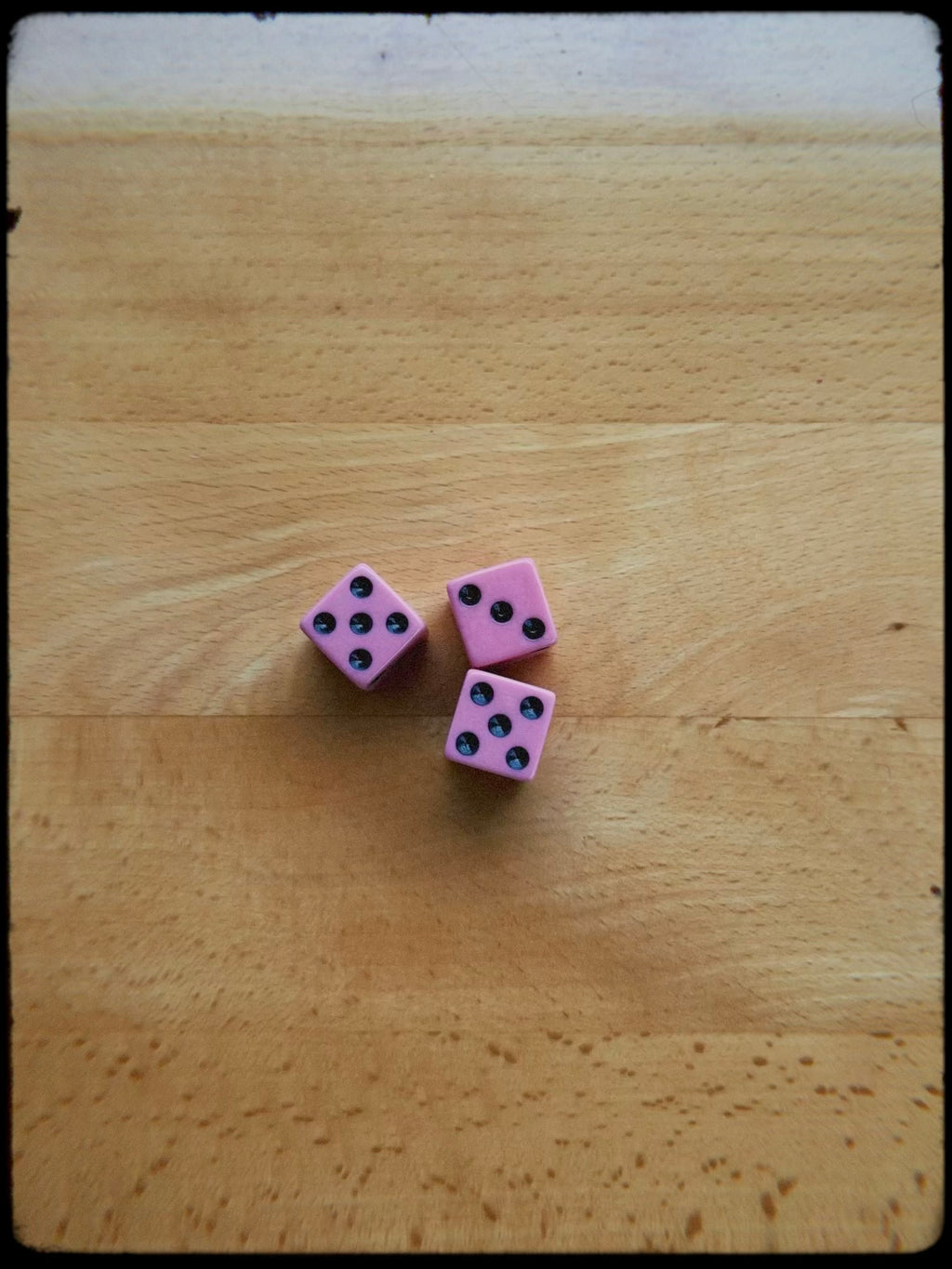 Three pink dice with black dots on a wooden surface
